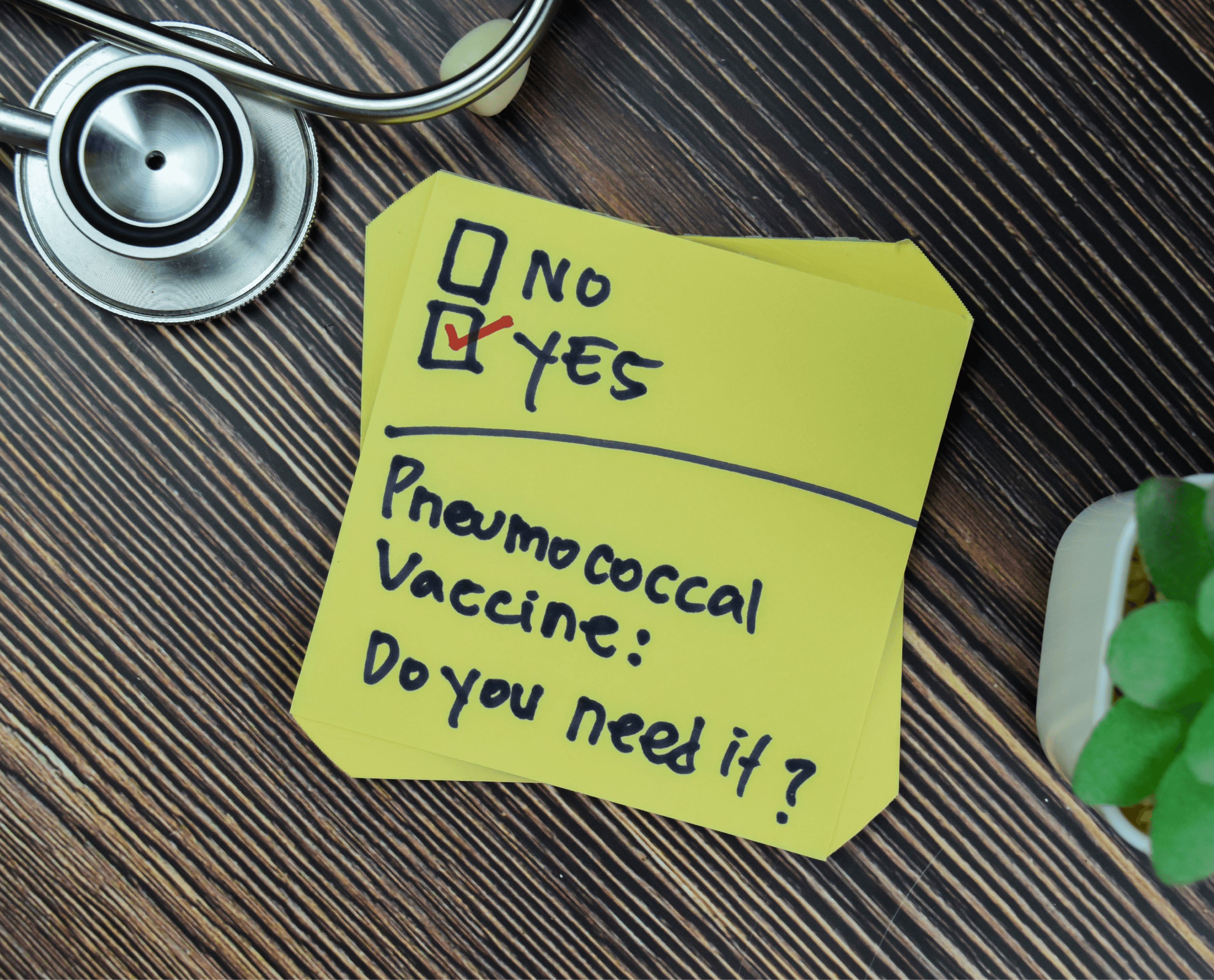 A stethoscope and a yellow sticky note with a checklist and text 'Pneumococcal Vaccine: Do you need it?' on a wooden table